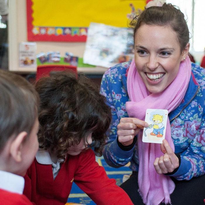 Young woman holding a card with cartoon bear and smiling at group of schoolchildren