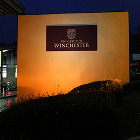 University of Winchester sign on wall lit with orange light