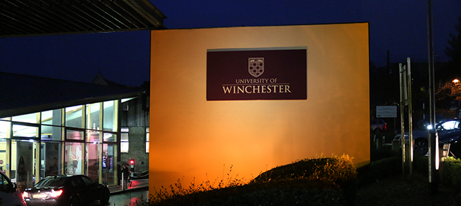 University of Winchester sign on wall lit with orange light