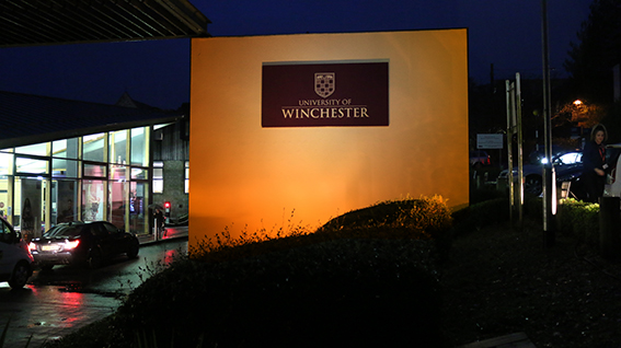 University entrance sign lit up by orange light