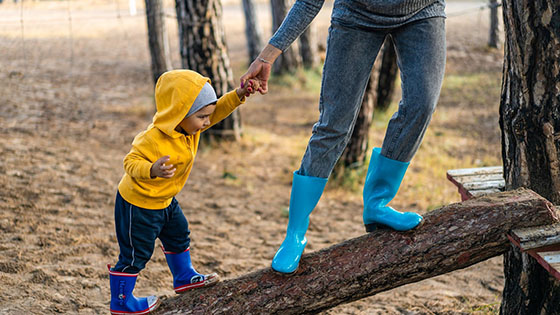 Small boy walks along a log holding his mother's hand