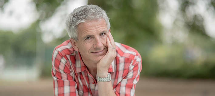 Man in checked shirt leaning on a gate with his chin resting on his hand