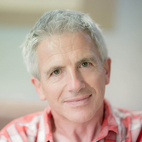 Man in checked shirt leaning on a gate with his chin resting on his hand