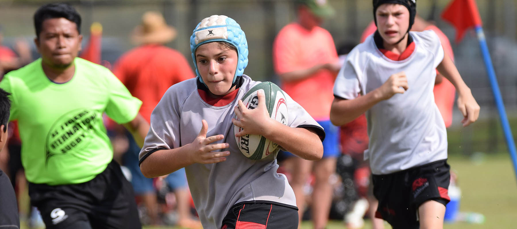 Young rugby player holding ball and running down the pitch chased by another player