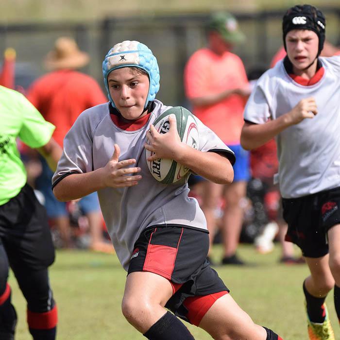 Young rugby player holding ball and running down the pitch chased by another player