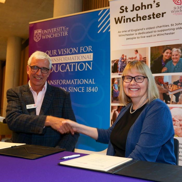 Group of people standing behind desk and in front of university and St John's banners