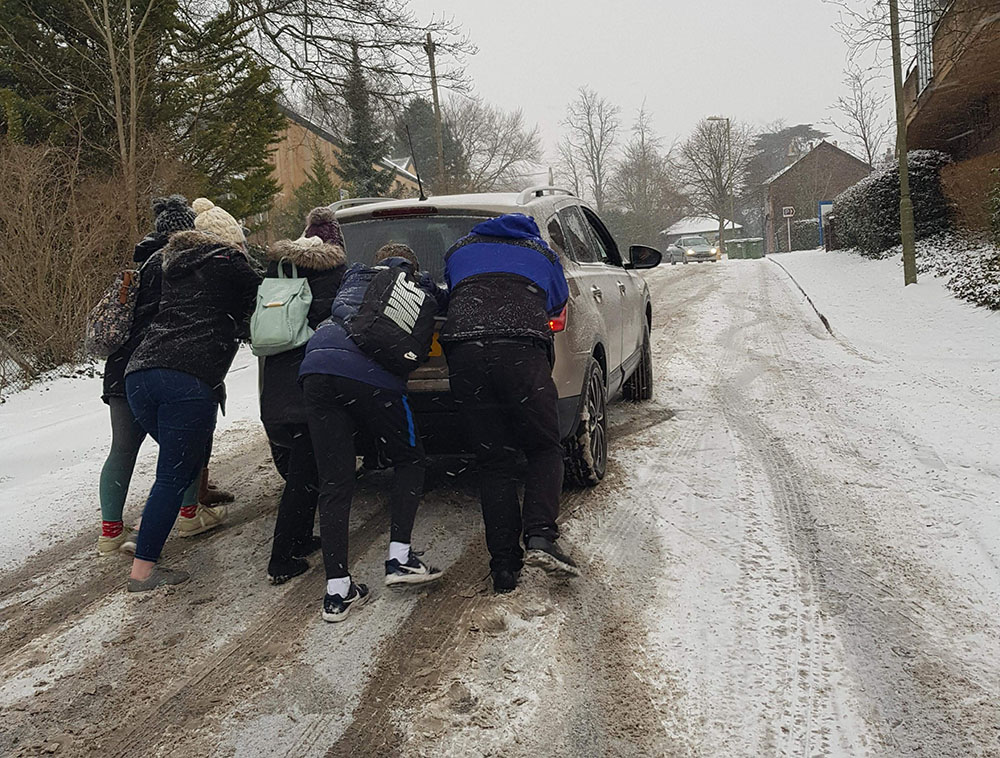 People pushing car uphill on a snowy road