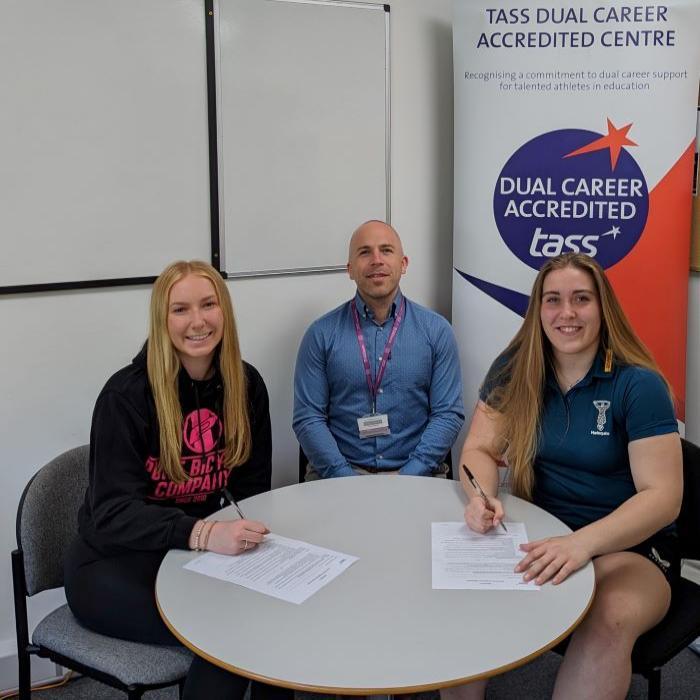 Two girls signing documents as man in middle look on