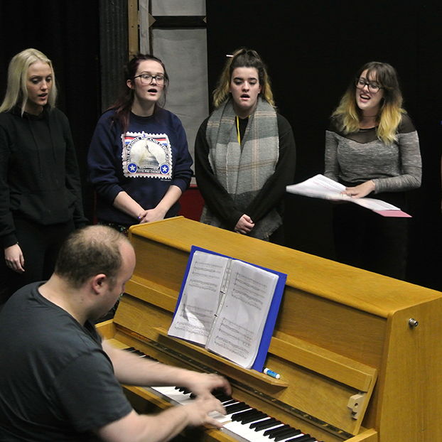 Group of people singing around a piano