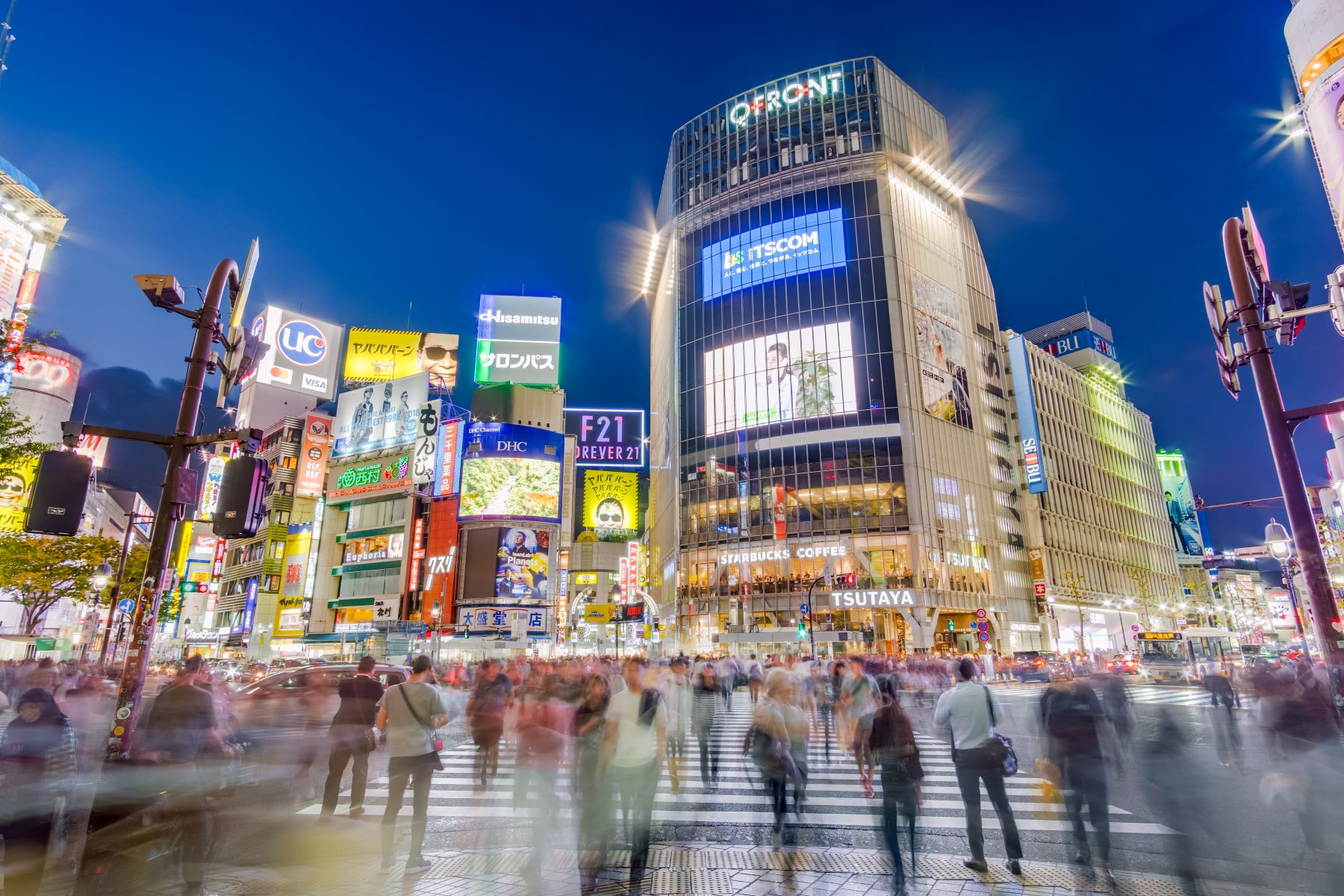 A busy nightime street scene in Tokyo. Images of people and cars moving are blurred