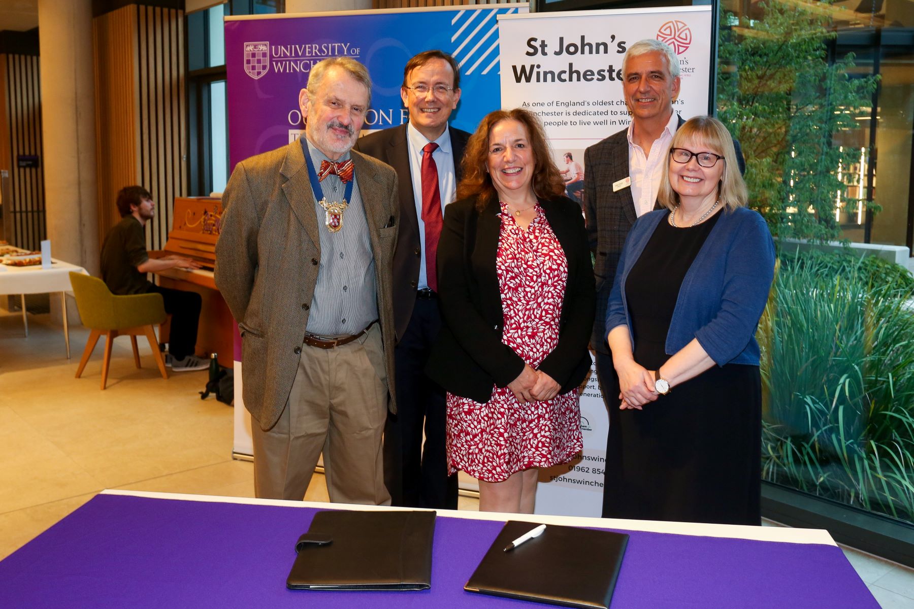 Group of people standing behind desk and in front of university and St John's banners