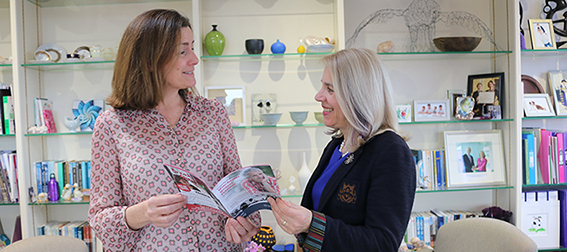 Two women standing in front of bookcase look at brochure 