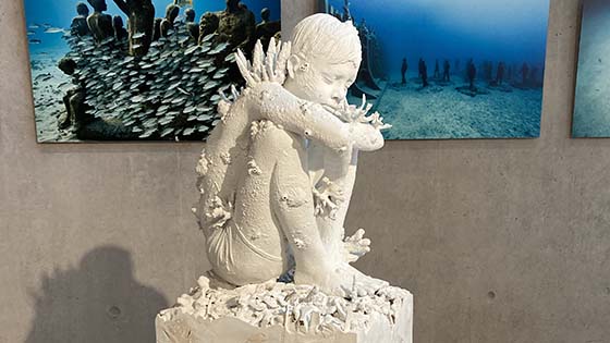 White sculpture on a plinth of young boy sitting hugging his knees