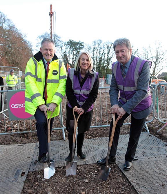 Three people in high vis jackets with spades digging a hole in the earth