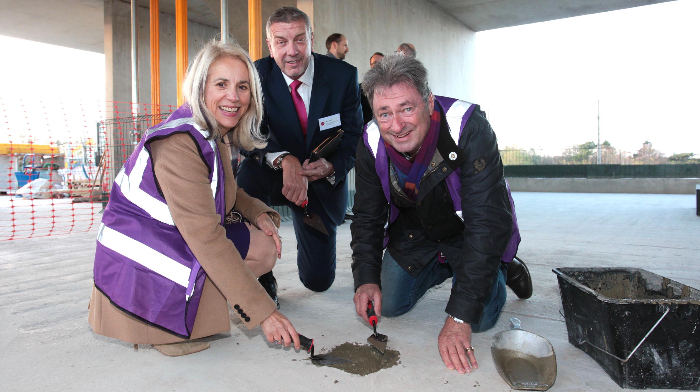 Three people crouching inside a building under construction placing concrete in a small hole with trowels