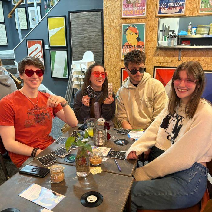 Four young people, two male two female, sat at table playing bingo