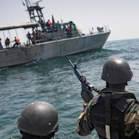 Soldiers in small craft point guns at men in inflatable boar