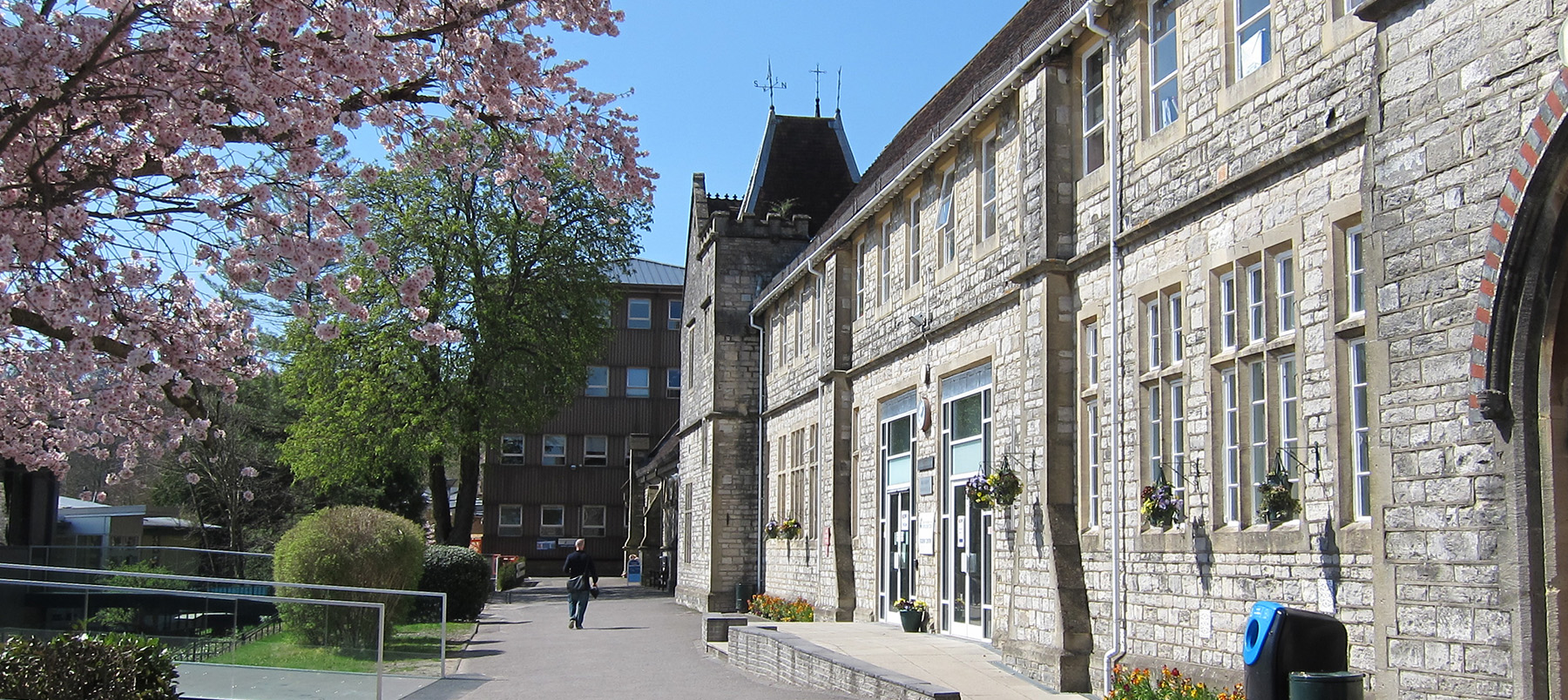 View of Victorian stone building with path running by it and a pink cherry tree in blossom against a blue sky