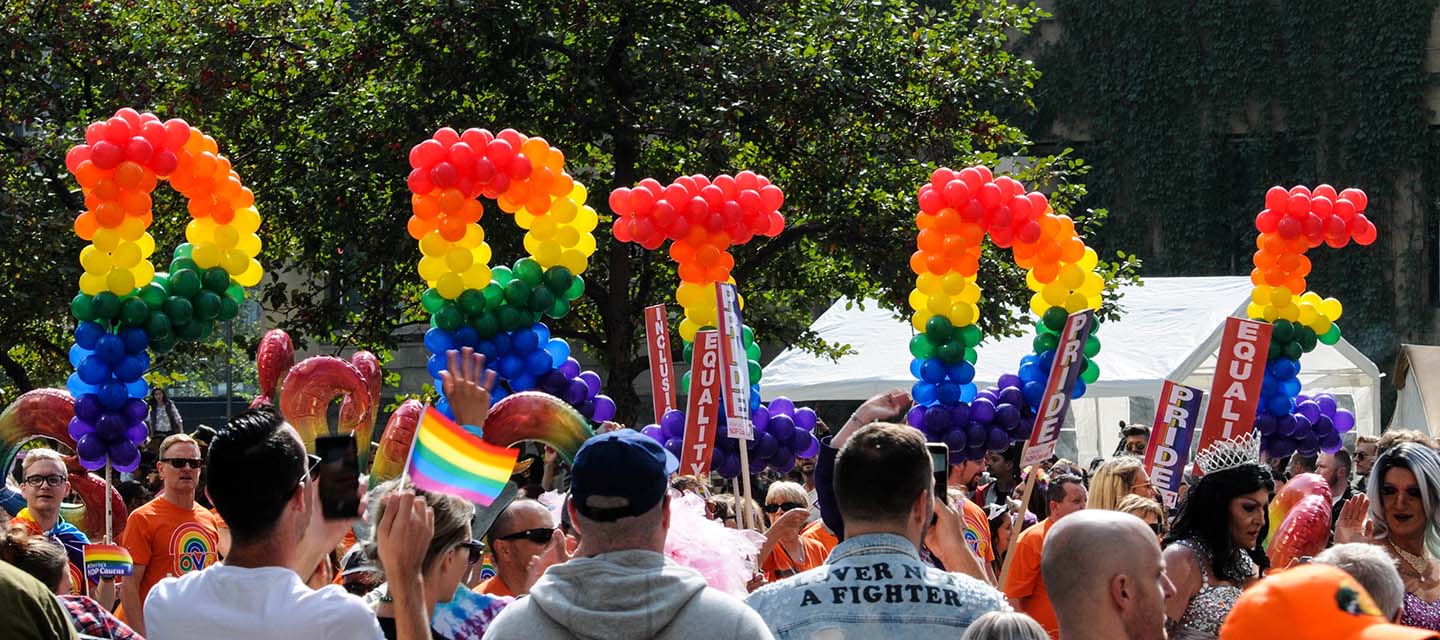 The letters for 'Pride' spelt out in rainbow balloons, held by pride supporters