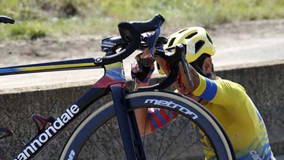 Cyclist in yellow jersey sitting injured on the road holding his bike