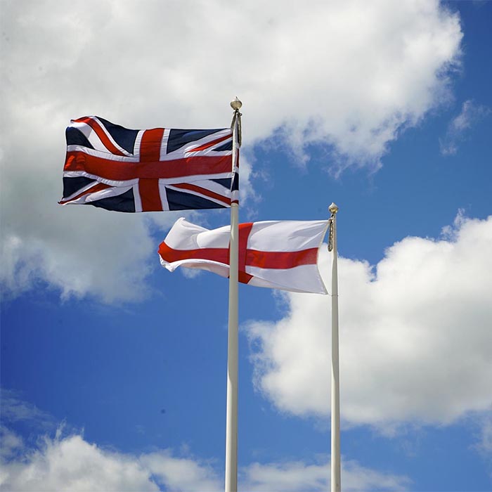 English and British flags fly side by side against blue skies