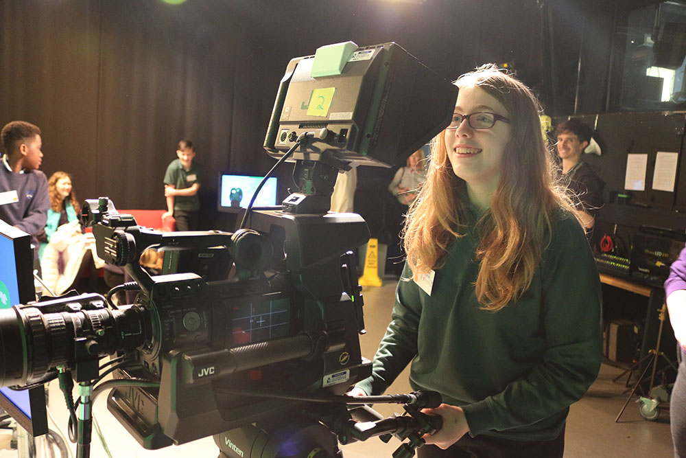 Student smiles looking through large filming camera