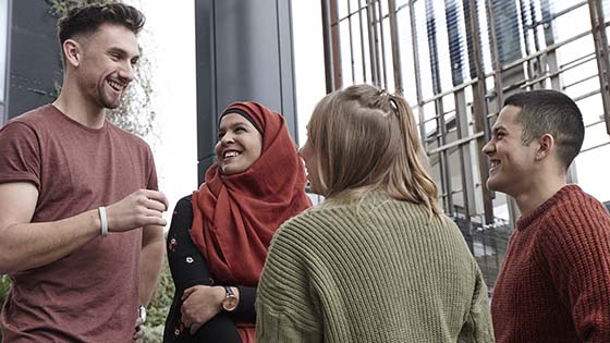 Group of four students smiling and talking outside building