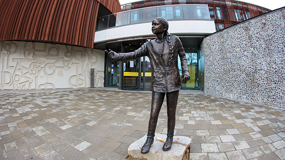 bronze sculpture of greta thunberg holding out her hand in front of entrance to modern building