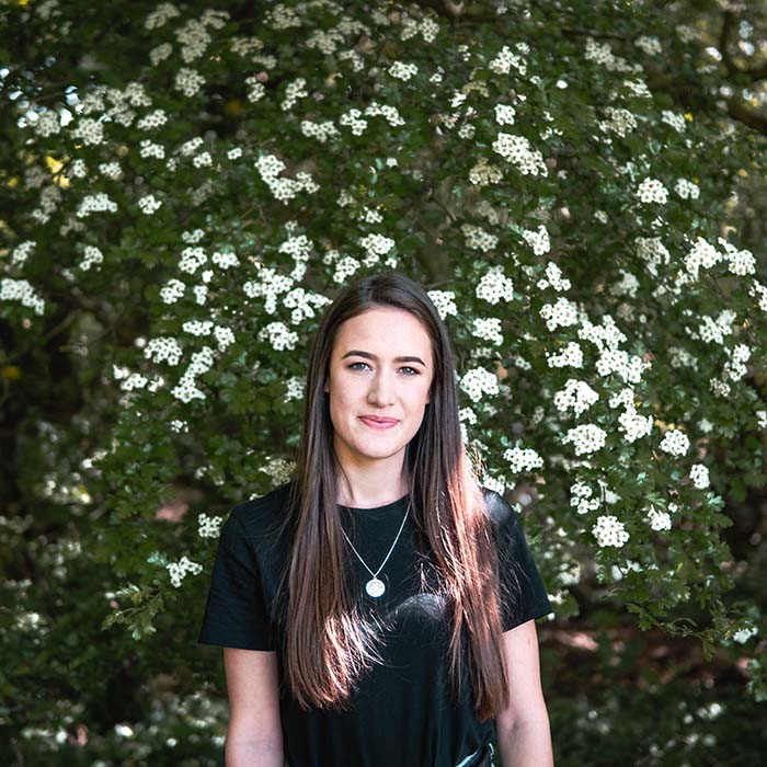 Young woman with long dark hair standing in front of the flowering hedge