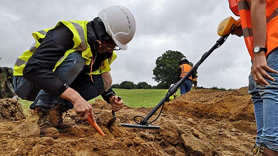 People in high-vis sorting through mud - one has metal detector