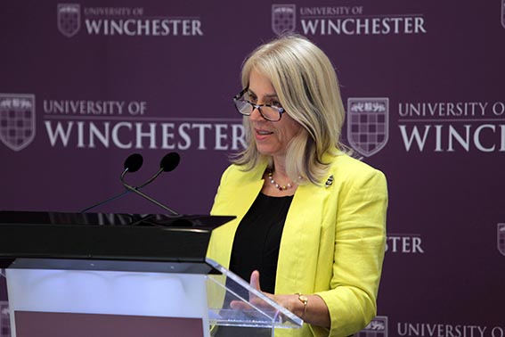 Professor Joy Carter in a yellow blazer speaking at podium