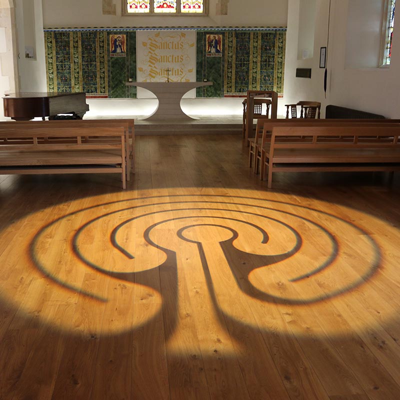 Light projection of a Labyrinth, a continuous line that weaves back on itself, on wooden floor of University of Winchester Chapel