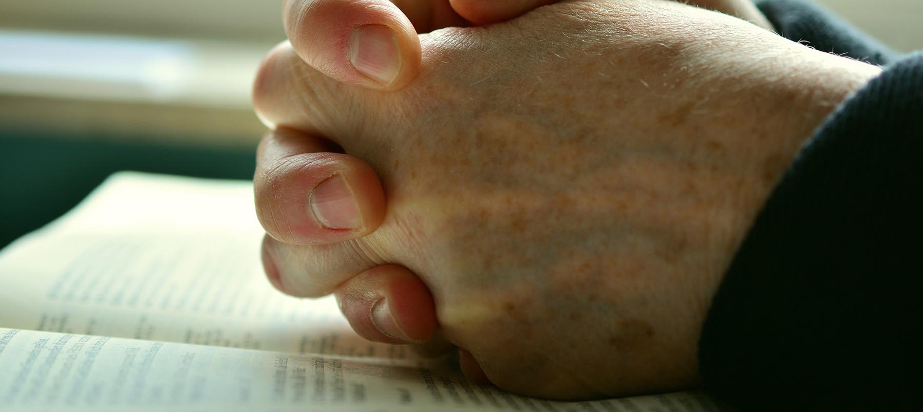 Hands clutched in prayer over an open bible