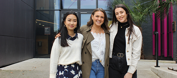 Fashion and lifestyle influencer Monica Welburn stands outside smiling with two Winchester students