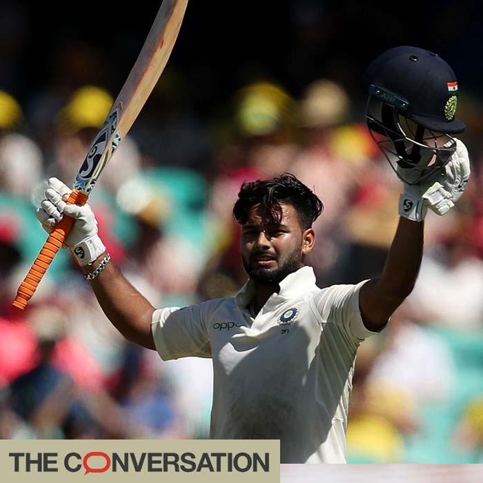 Cricketer Rishabh Pant holding his bat and helmet aloft on the field of play