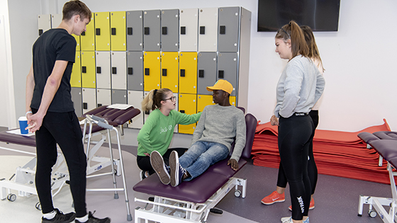 Male student lying on treatment couch talking to four other physiotherapy students