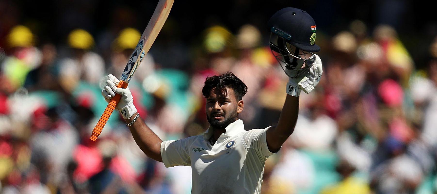 Cricketer Rishabh Pant holding his bat and helmet aloft on the field of play