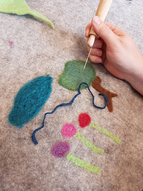 Person felting tree, cloud and flowers with needle on cloth
