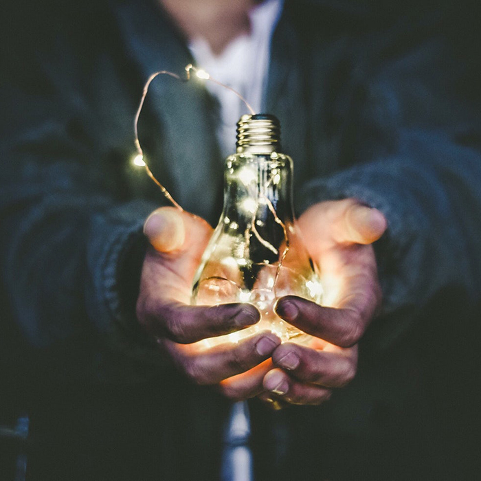 Close up of hands holding lightbulb with fairy lights inside