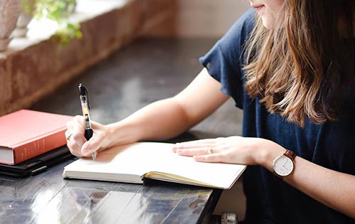 Woman writing in book on black countertop