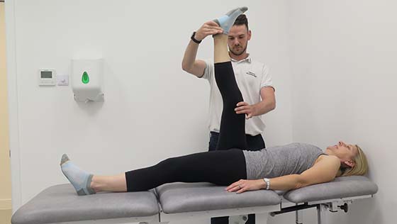 Physiotherapist supporting patient's leg as she lies on a treatment couch