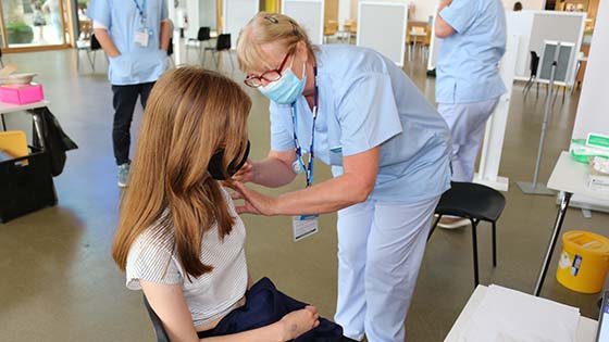 Nurse vaccinating young woman sitting down