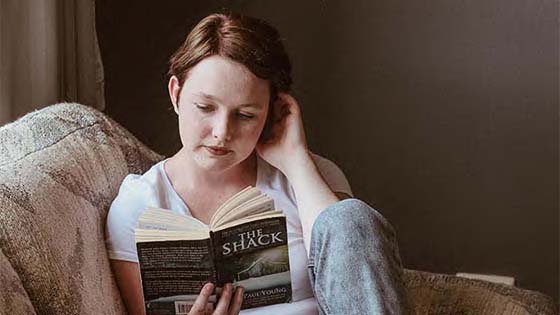 young woman sitting on sofa reading a book