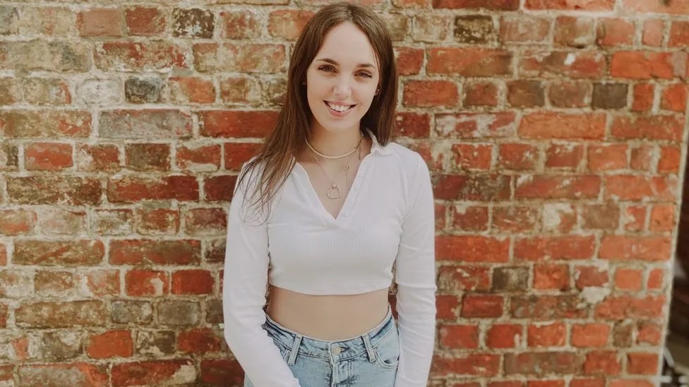 Young woman with long dark hair standing in front of brick wall