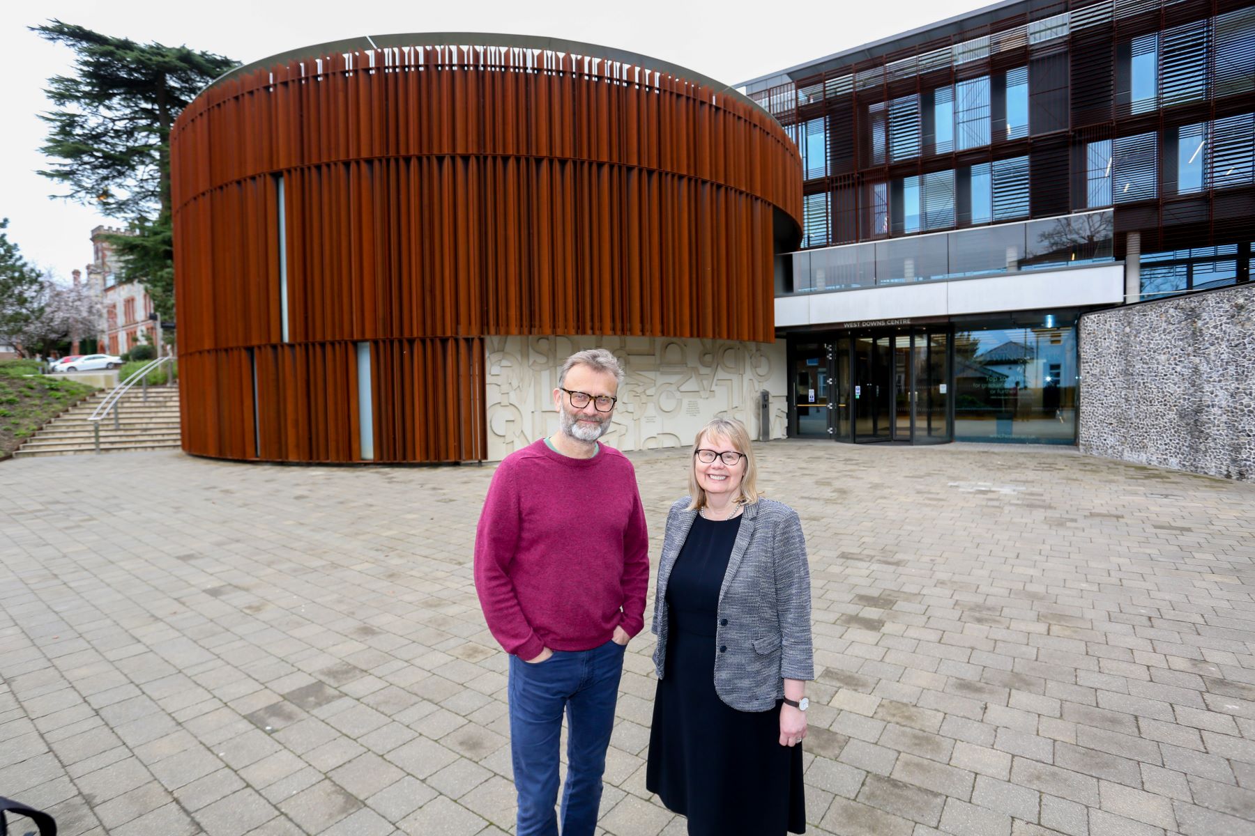 Man and woman in front of large rusty brown building