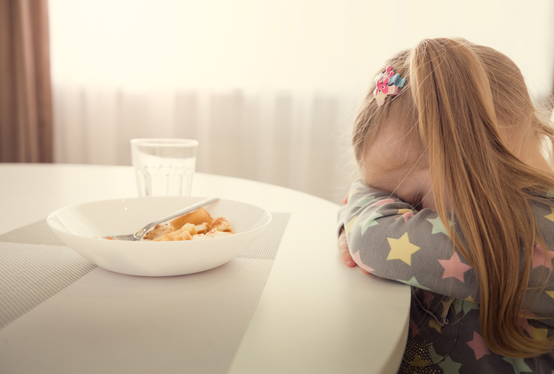 Child sitting at table not wanting to eat her meal