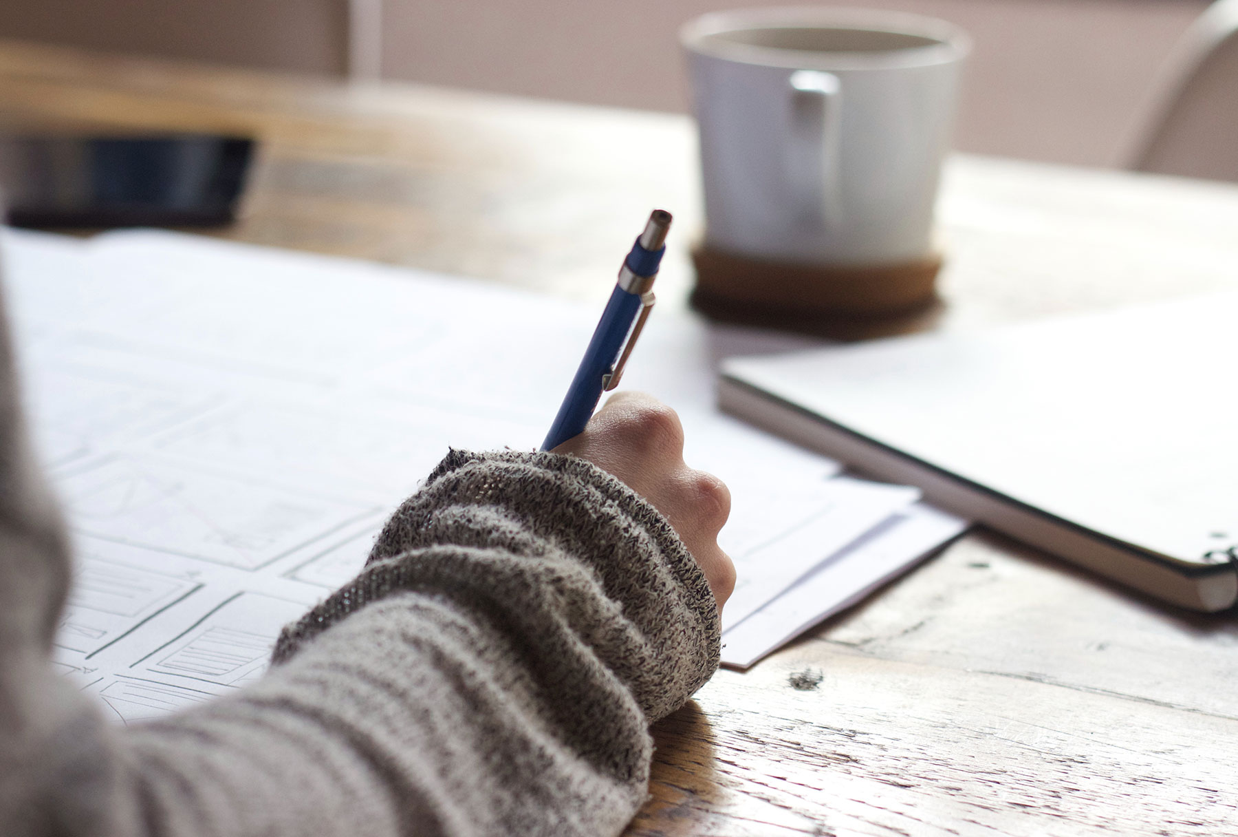 Person making notes on a piece of paper with a cup in front of them