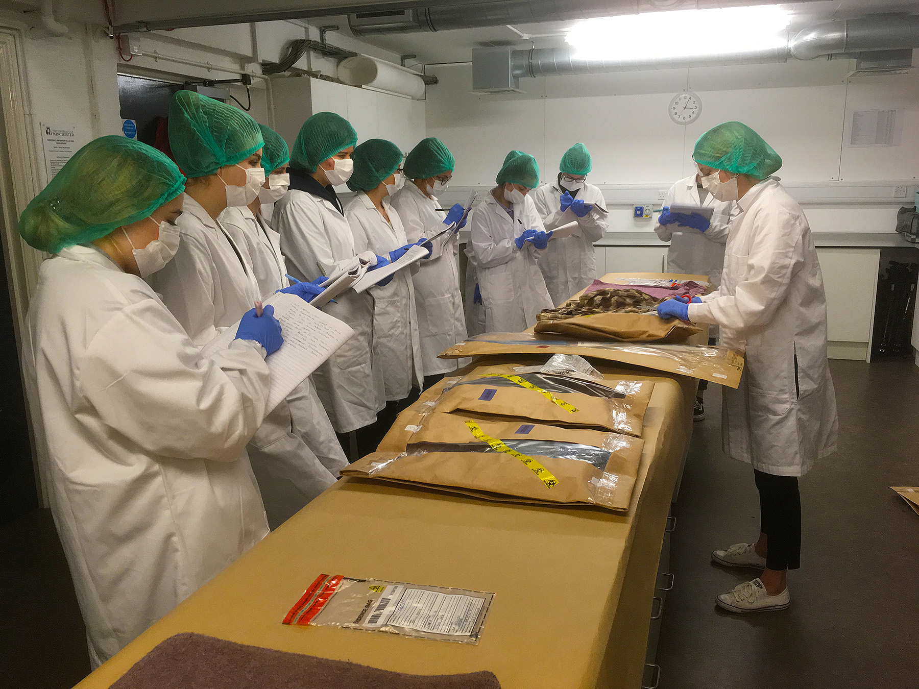 Room of students in lab coats looking at bags of evidence