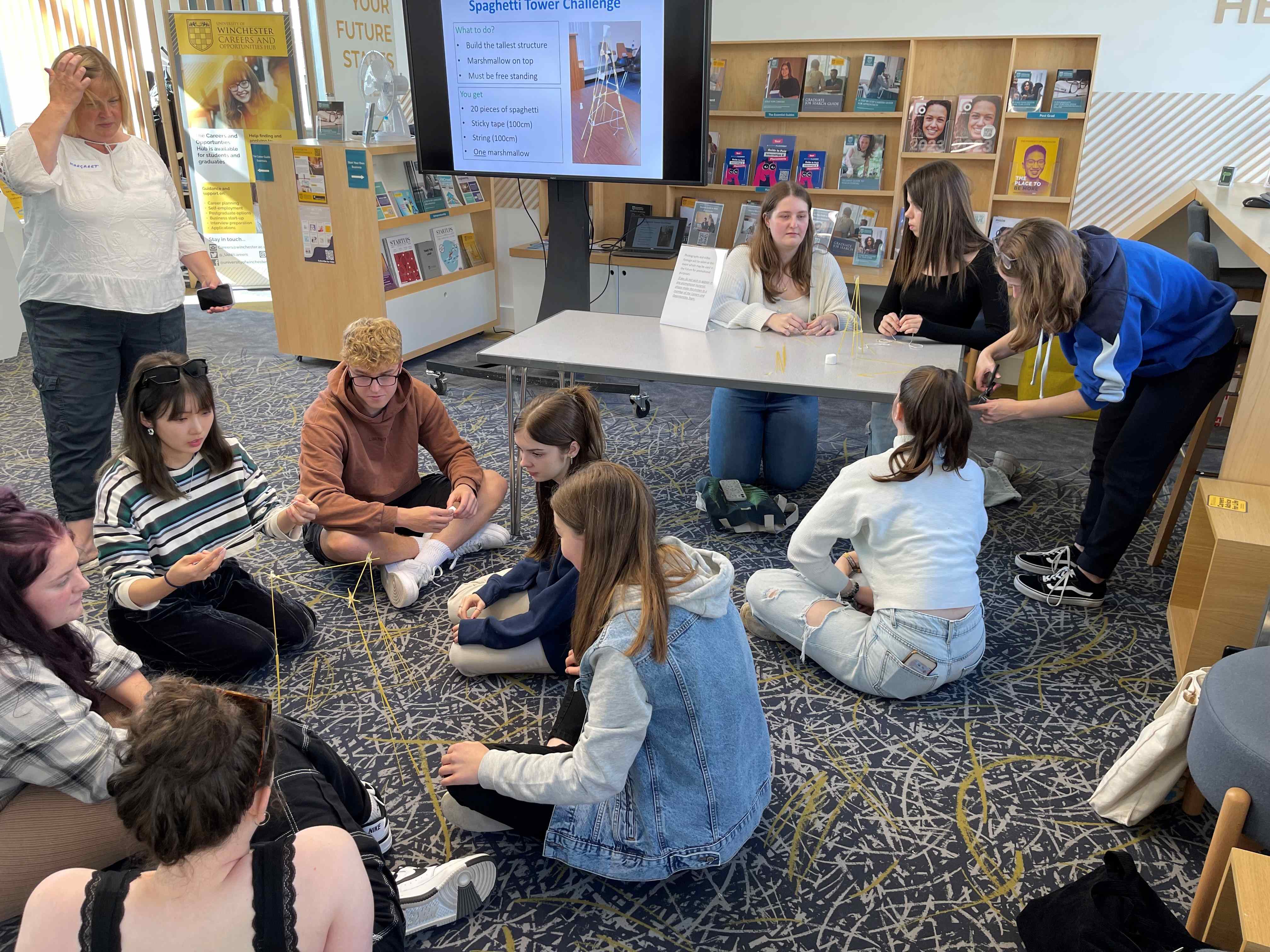 Students sitting on the floor building towers from dry spaghetti