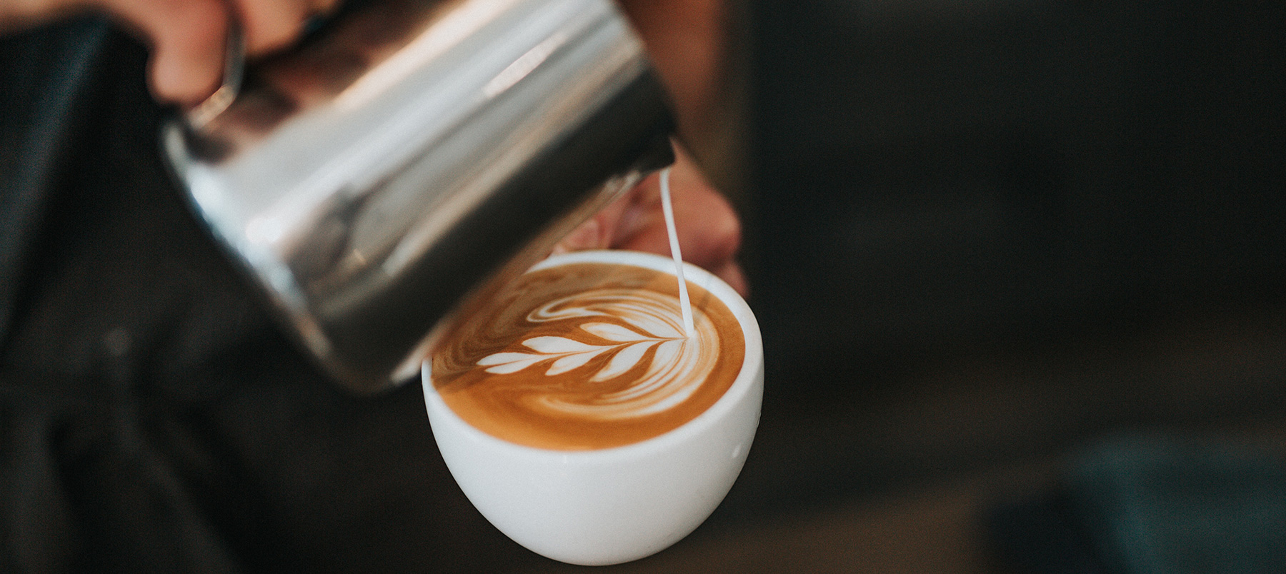 Milk being poured into a coffee mug in the shape of a leaf